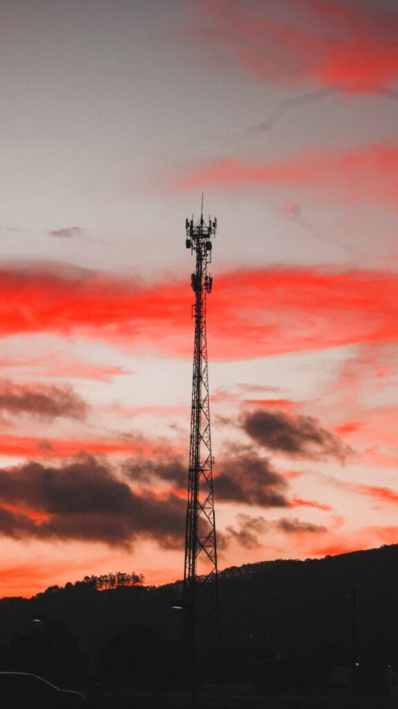 Dramatic silhouette of a telecommunication tower against a vivid red sunset sky.